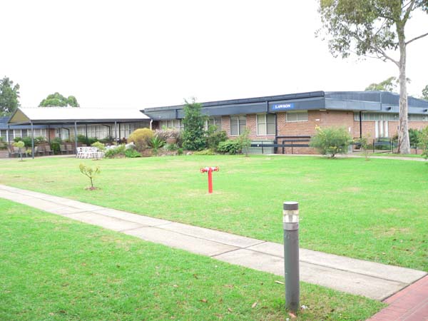 Grass area with large accommodation building in the background. Lawson sign is on the roof. There is a large tree to the right.