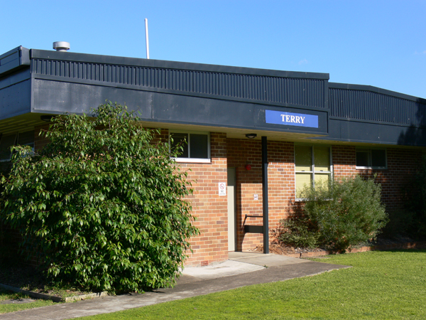 Single storey brick accommodation block entry. There is a bush on either side of the door and Terry sign above the door.