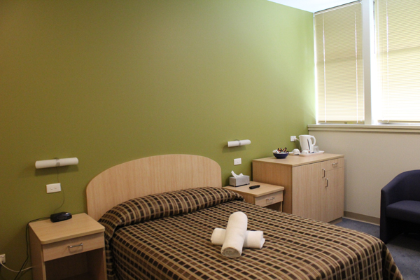 Accommodation room with green feature wall, and bed in centre of the room. Two bedside tables are on either side of the bed and a tea/coffee preparation area is on the right.