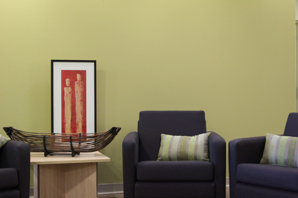 Three single seat lounges in front of green feature wall. Side table with two artworks sitting on it.