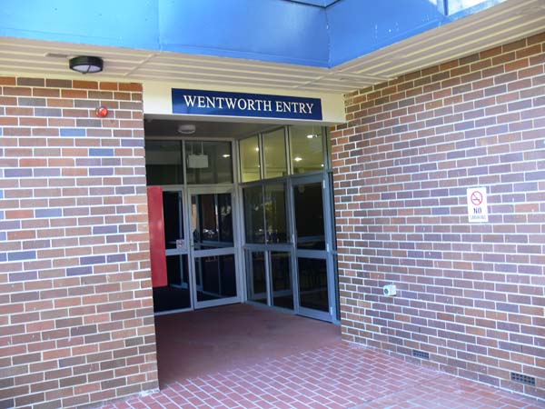 Single storey brick accommodation block entry. Courtyard leads to glass door entrance. Wentworth entry sign is located above the doors.