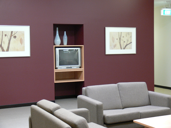 Room with two 2-seater lounges and coffee table. Burgundy feature wall housing small TV and two artworks to either side.