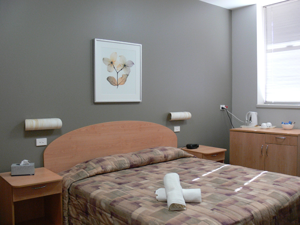 Bedroom with grey feature wall. Bed central to room with bedside tables. Tea/coffee preparation area on right of room.