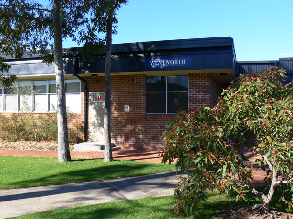 Single storey brick accommodation block external view. Wentworth sign is above window. Trees and bushes are in front of the building.