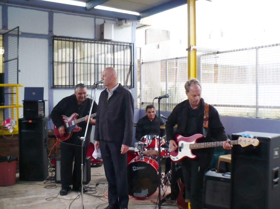 Murray Cook playing the guitar standing next to Peter Garret and the Midnight Oil rock band. 