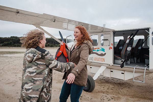 Two adult females hugging next to a plane