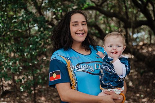 A young female holding a toddler smiling and happy