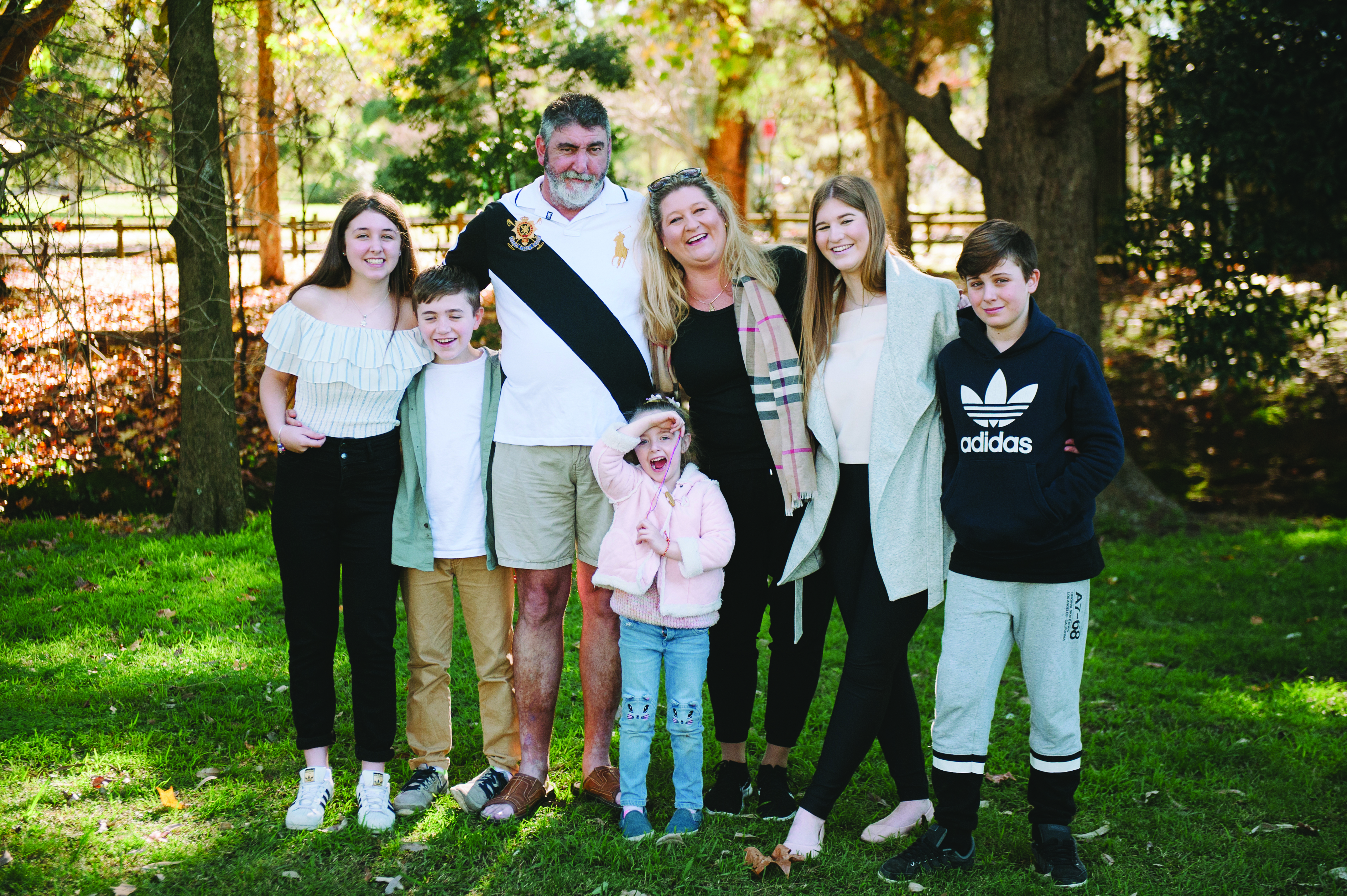 An adult male and female smiling and standing with their arms around their five young children who are also all smiling happily