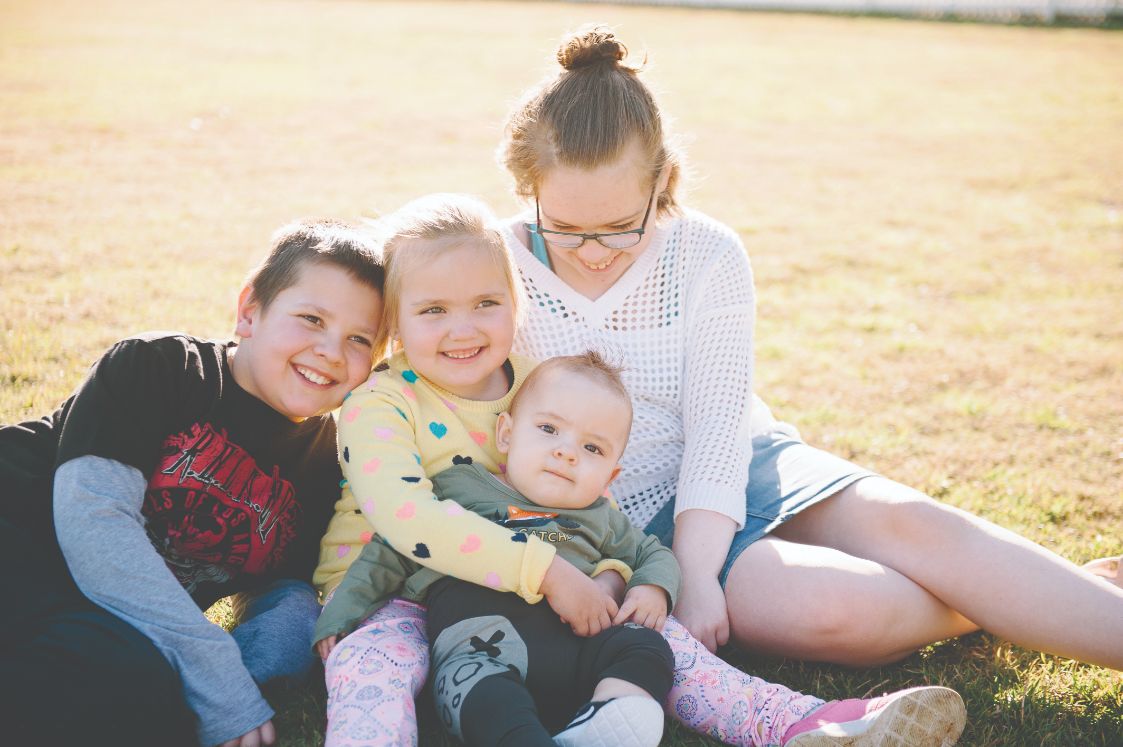 The young children holding a small toddler whilst smiling