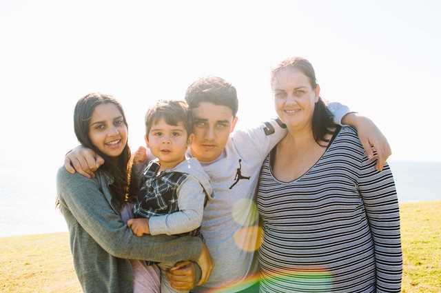 An adult female with two teenagers and one young child standing side by side with their arms around each other smiling