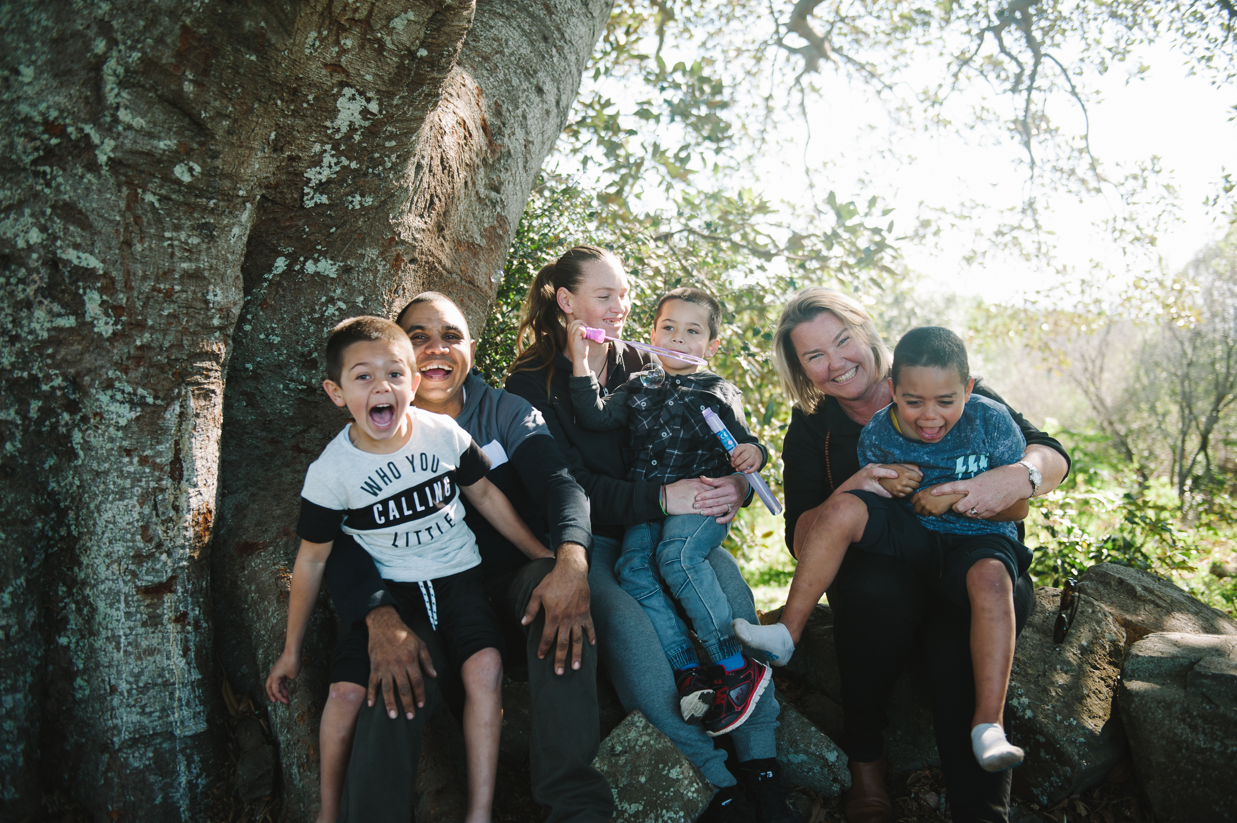 Three children sitting on the laps of three female adults smiling and having fun playing. 